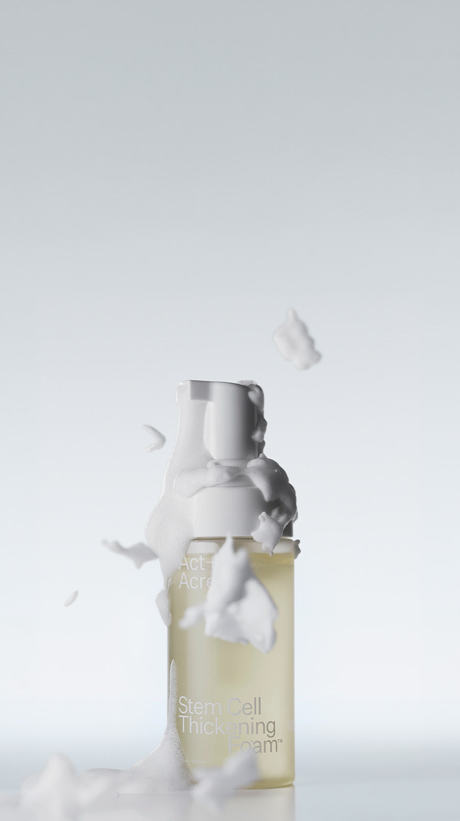 A bottle of foam hair product with white foam splashing around it, set against a light gray background.